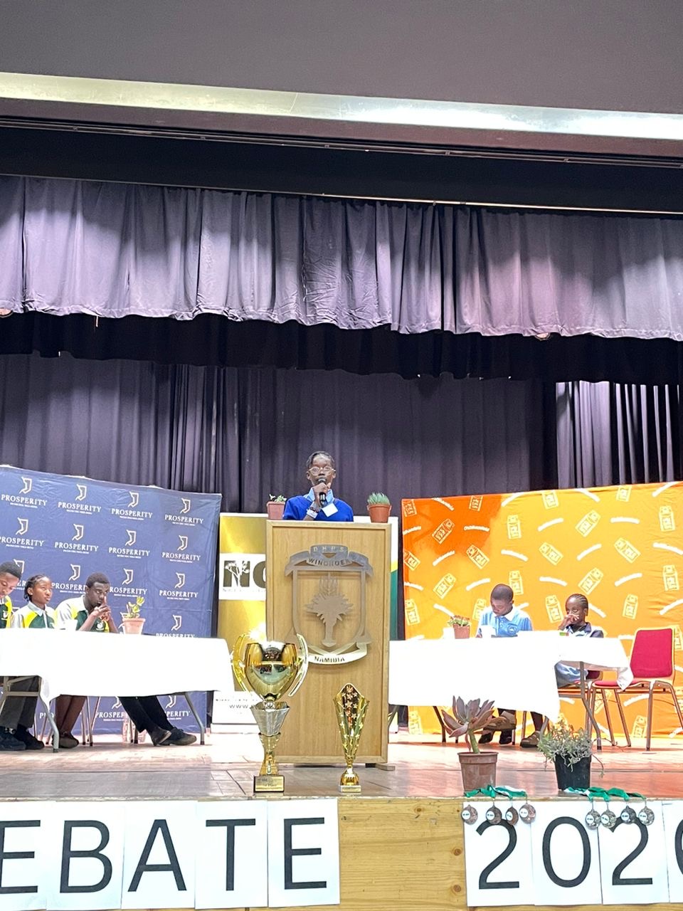 Debate finals on stage at DHPS with judges and trophies