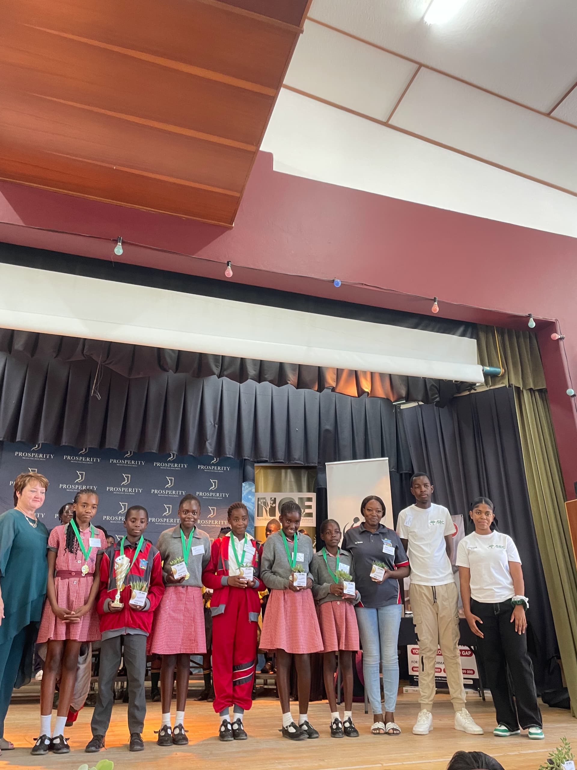 Quiz award ceremony with learners holding medals and plants on stage