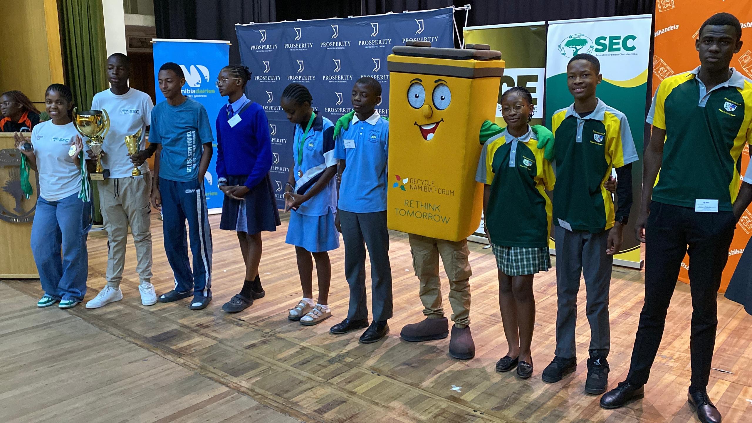 Quiz finalists lined up on stage with trophies and the recycling mascot