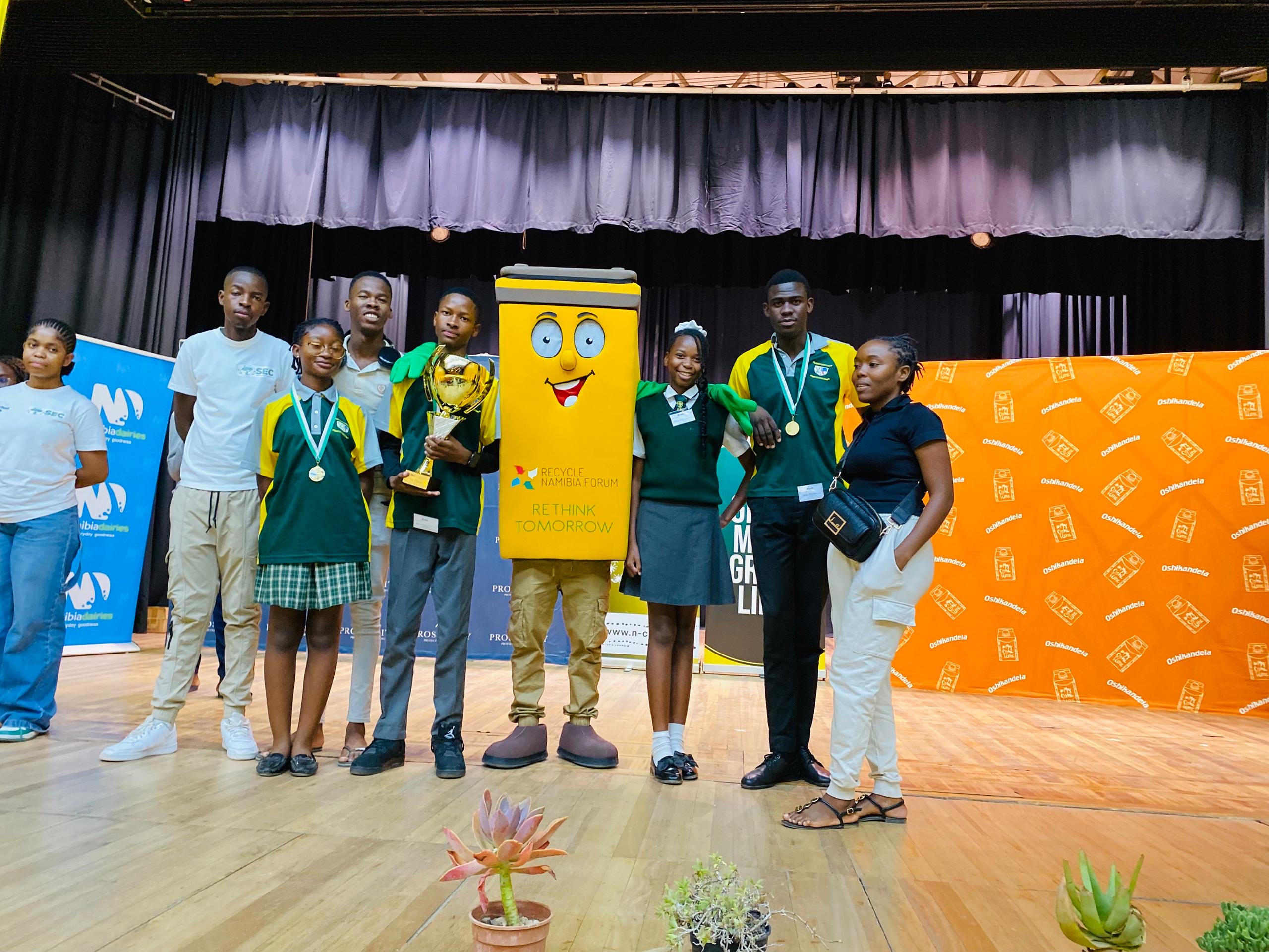 SEC Namibia learners on stage with medals and the Recycle Namibia Forum mascot at the Primary Schools Quiz